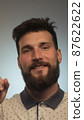 Portrait of bearded young male model rejoices coming weekends, dressed casually. Cheerful guy smiles happily, has excited expression, celebrates his anniversary or promotion at work 87622622