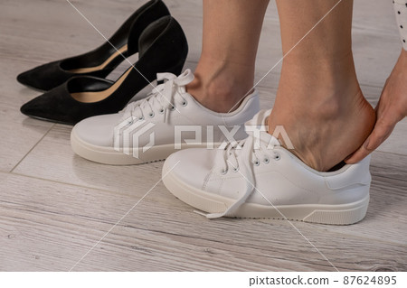 Close-up business woman takes off her shoes puts on white leather sneakers. 87624895