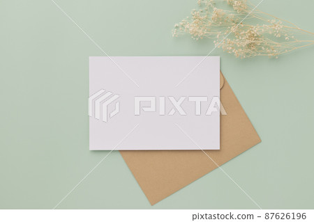 Blank greeting card invitation Mockup 5x7 on Brown envelope with dried flowers on pastel green background, flat lay, mockup 87626196