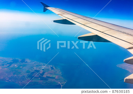 View from the airplane window at a beautiful blue clear sky, earth, sea and the airplane wing View from the airplane window at a beautiful blue clear sky, earth, sea and the airplane wing 87630185