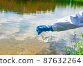Analysis, water sample from the river, lake. A gloved hand collects water in a test tube. 87632264