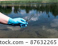 Analysis, water sample from the river, lake. A gloved hand collects water in a test tube. 87632265