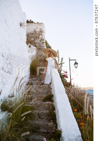 young elegant woman wearing straw hat and white dress standing on stars at old town - Greece, Spetses young elegant woman wearing straw hat and white dress standing on stars at old town - Greece, Spetses 87637247