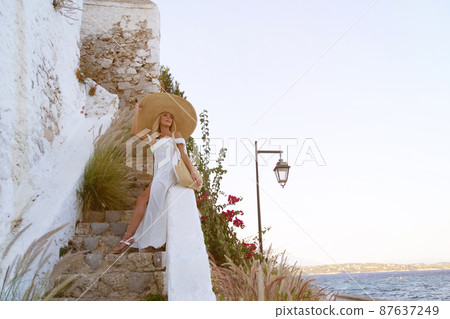 young elegant woman wearing straw hat and white dress standing on stars at old town - Greece, Spetses young elegant woman wearing straw hat and white dress standing on stars at old town - Greece, Spetses 87637249