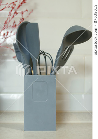Silicone kitchenware such as ladles, spatulas and whisk in a stand on a home kitchen table 87638015