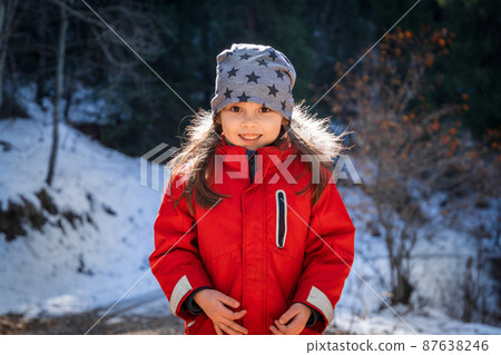 Portrait of 5 - 7 y.o. happy girl wearing red jacket in winter sunny day 87638246