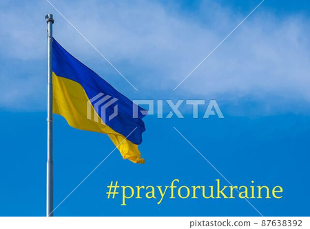 hashtag PRAY FOR UKRAINE text on Ukrainian national flag flutters in the wind against the blue sky. National symbol of ukrainian people - blue and yellow. No war. War Protest against Russian invasion 87638392