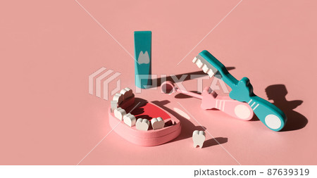 A wooden model of a jaw with a lost molar tooth and tools for daily dental care, examination and prevention of caries on a pink background. Dental concept banner with copy space. Children's toy doctor 87639319