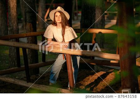 Tween girl standing in animal stall in green summer country estate Tween girl standing in animal stall in green summer country estate 87643158