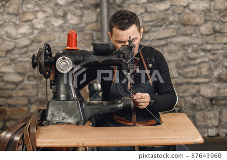 Leather craftsman working on a belt using a sewing machine 87643960