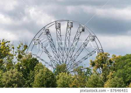 View of ferris wheel between trees. View of ferris wheel between trees. 87646481