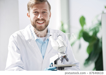 smiling scientist sitting at a laboratory table. 87646610