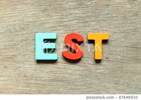 Color alphabet letter in word EST  (abbreviation of established, estimated, eastern time zone, expressed sequence tag) on wood background 87646910