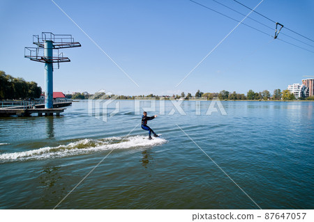 Wakeboarder surfing on lake. Young surfer having fun wakeboarding in the cable park. Aerial view. Water sport, outdoor activity concept. 87647057