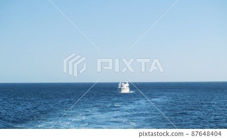 White motor yacht sailing alone across sea, clear sky above horizon. Luxury sea voyage, view from boat. Motor trail on clean water. Nice sunny day for holiday small waves on marine surface 87648404
