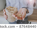 a woman's hand holds a handful of oatmeal and a glass jar  87648440