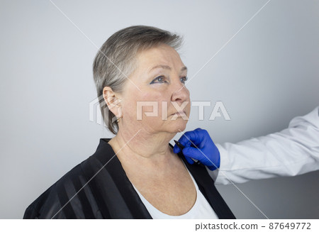 An elderly woman at the reception of a facial plastic surgeon. Consultation on the removal of age wrinkles on the face. The doctor shows what procedures he will do. Mimic wrinkles. Contour plastic 87649772