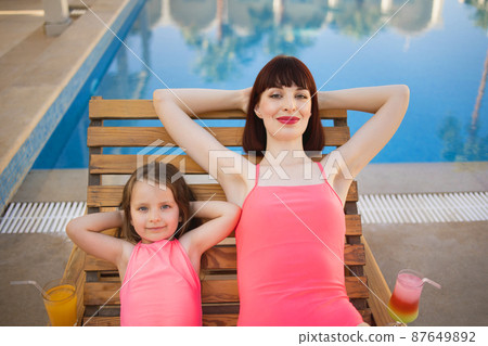 Woman with cute daughter joyful lying with pleasure on wooden deck chair. Woman with cute daughter joyful lying with pleasure on wooden deck chair. 87649892
