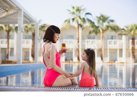 Back view of happy caucasian mother holding her daughter's hand are enjoying swimming in pool Back view of happy caucasian mother holding her daughter's hand are enjoying swimming in pool 87650066