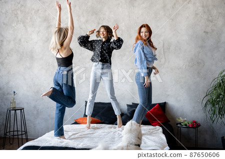 Adult girlfriends having fun, jumping together on bed at home 87650606