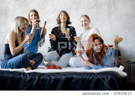Adult girlfriends having fun, sitting together on bed at home Adult girlfriends having fun, sitting together on bed at home 87650615
