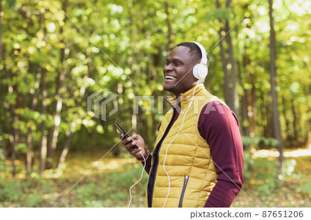 African american man listens music in spring park copy space and place for advertising. Gadget, app and streaming service concept African american man listens music in spring park copy space and place for advertising. Gadget, app and streaming service concept 87651206