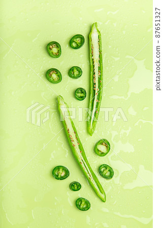 Pieces of green chili peppers lying on color background with water drops 87651327