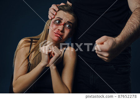 Cruel male put his hand on woman head. Scared victim with bruises on face sitting nearby, terrified. Blue background. Domestic violence. Close-up Cruel male put his hand on woman head. Scared victim with bruises on face sitting nearby, terrified. Blue background. Domestic violence. Close-up 87652278
