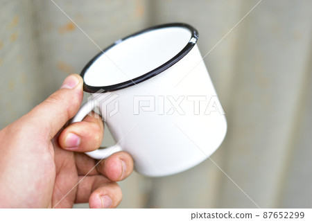 White metal enameled mug in the hands of a person 87652299