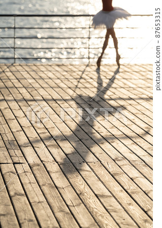 Shadow of blurred female ballet dancer on sunny wood pier Shadow of blurred female ballet dancer on sunny wood pier 87653315