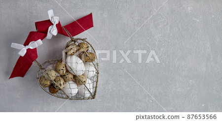 Chicken and quail eggs in a heart shaped woven metal wire basket 87653566