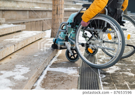 Woman in a wheelchair near the stairs in the park in winter. Woman in a wheelchair near the stairs in the park in winter. 87653596
