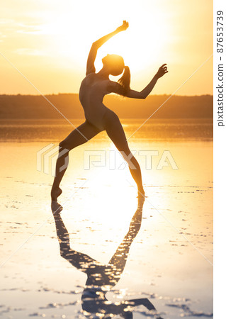 Female ballet dancer is posing in lagoon opposite sun shining sky Female ballet dancer is posing in lagoon opposite sun shining sky 87653739