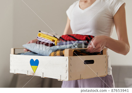 Help volunteering donation concept. A woman holding a donation box full of clothes at home 87653941
