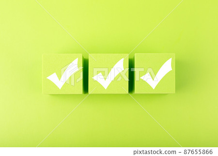 Three white checkmarks on green toy cubes in a row against bright green background. Checklist concept 87655866