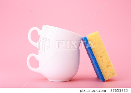 Creative, minimal dishwashing concept, yellow cleaning sponge next to two white ceramic cups on pink background Creative, minimal dishwashing concept, yellow cleaning sponge next to two white ceramic cups on pink background 87655883