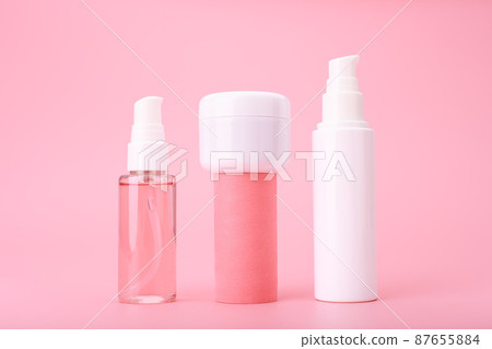 Set of beauty products in a row on white table against pink background. Face cleansing foam, cream and lotion 87655884