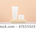 White cosmetic tubes with scrub and mask for face or hand skin on gypsum podium on white table against beige background.  87655929