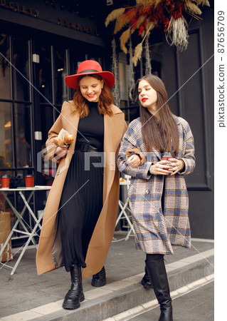 Two young girls standing near outdoor cafe holding a coffee and baguettes 87656709