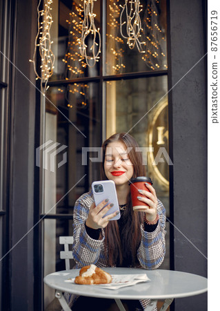 Girl with red lips sitting in a cafe outdoors and drinking coffee Girl with red lips sitting in a cafe outdoors and drinking coffee 87656719