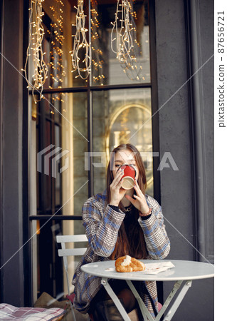 Girl with red lips sitting in a cafe outdoors and drinking coffee Girl with red lips sitting in a cafe outdoors and drinking coffee 87656721
