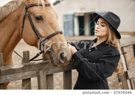 Woman touching a brown horse behinde the fence on a farm 87656846