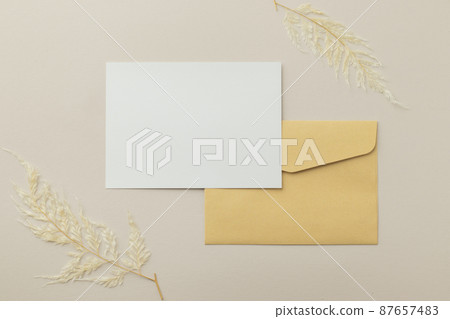 Blank greeting card invitation Mockup 5x7 on Brown envelope with dried flowers on beige background, flat lay, mockup 87657483
