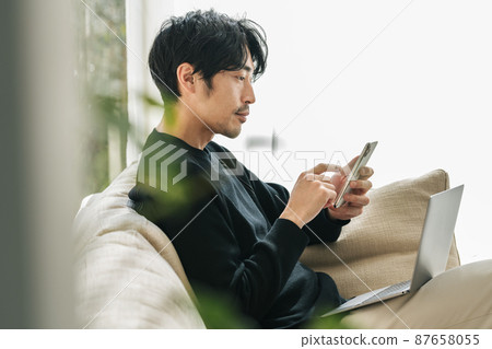 A man looking at a smartphone on the sofa at home A man looking at a smartphone on the sofa at home 87658055