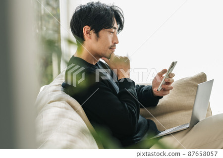 一個男人在家裡的沙發上看智能手機 87658057