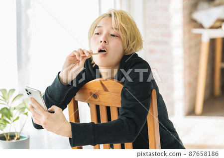 A woman brushing her teeth while holding a smartphone 87658186