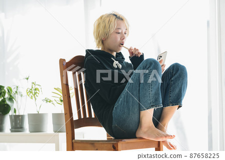 A woman brushing her teeth while holding a smartphone A woman brushing her teeth while holding a smartphone 87658225