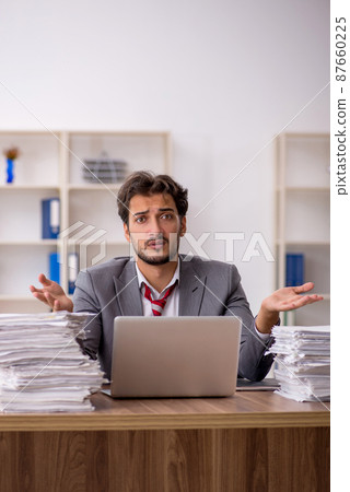Young male employee unhappy with excessive work in the office Young male employee unhappy with excessive work in the office 87660225