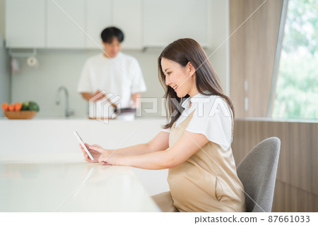 A man doing housework with a pregnant woman looking at a smartphone 87661033