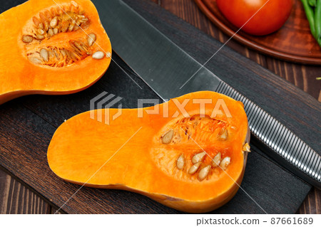 Small pumpkin cut into halves on wooden cutting board with knife 87661689